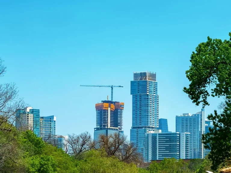City skyline with modern high-rise buildings and a construction crane, framed by green trees. water damage restoration Spring TX