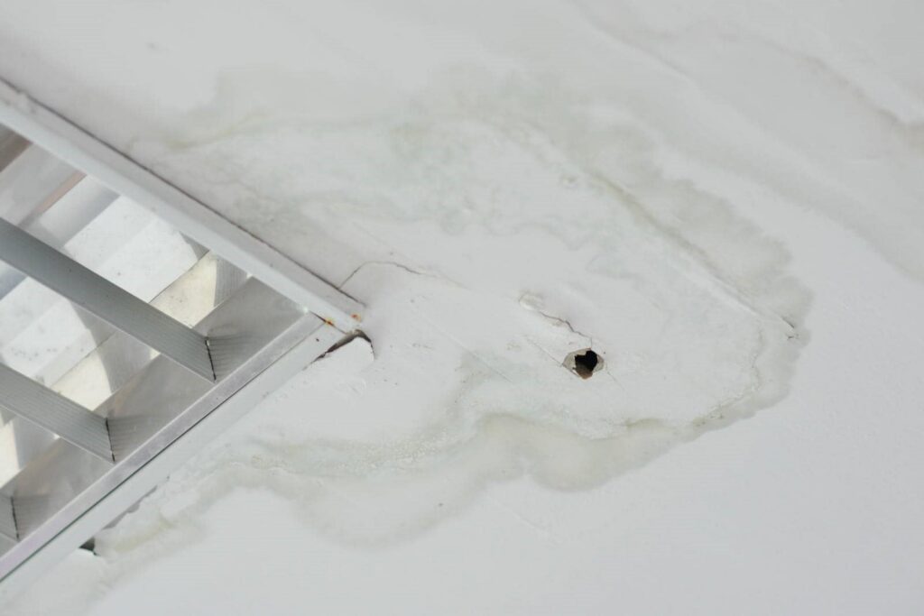 Water-stained ceiling with a small hole and metal air vent nearby.