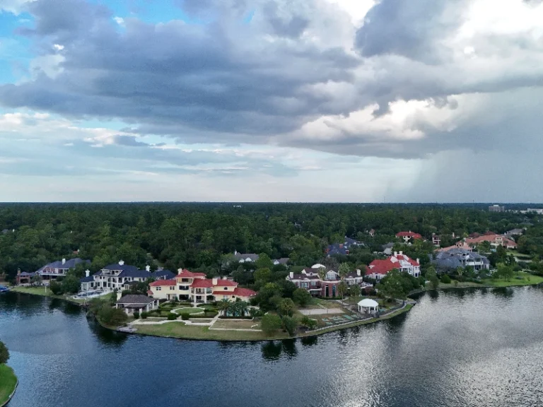 Aerial view of a lakeside neighborhood with large houses and cloudy sky above. water damage restoration The Woodlands TX