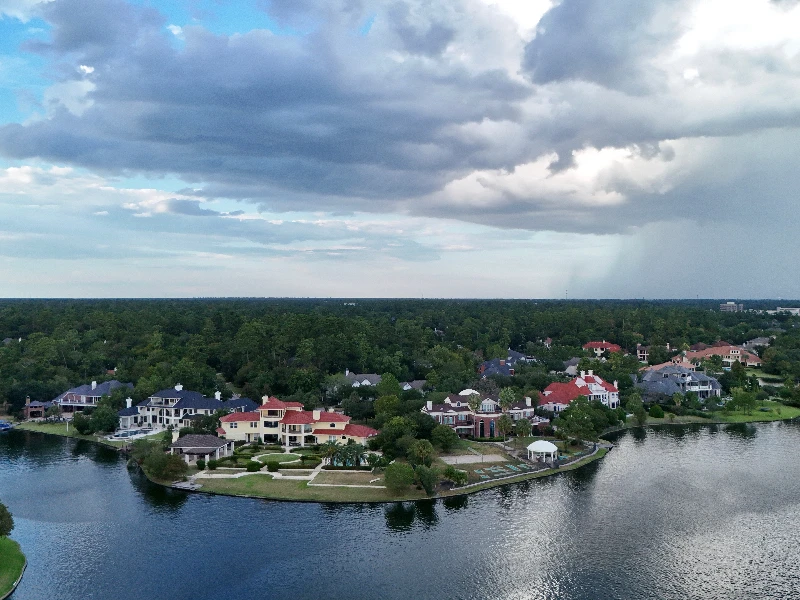 Aerial view of a lakeside neighborhood with large houses and cloudy sky above. water damage restoration The Woodlands TX