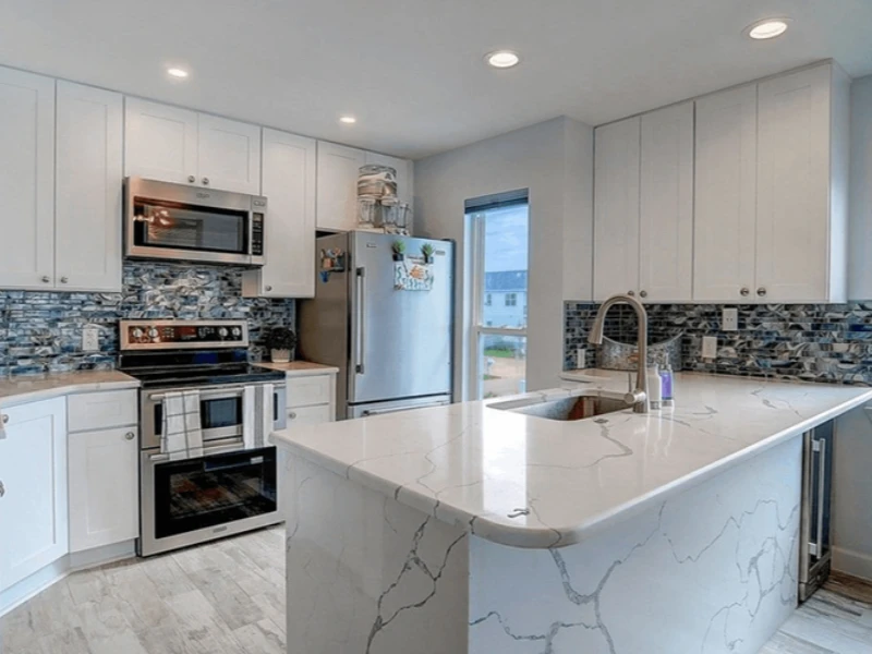 Modern kitchen with white cabinets, marble countertops, stainless steel appliances, and a window. water damage restoration company