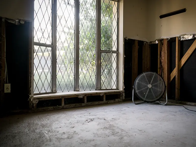 Large industrial fan on a bare concrete floor in a partially demolished room with diamond-patterned windows. commercial restoration services