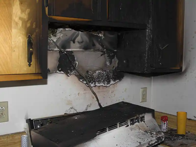 Burned kitchen cabinets and wall above a stove with fire damage and soot. fire damage restoration