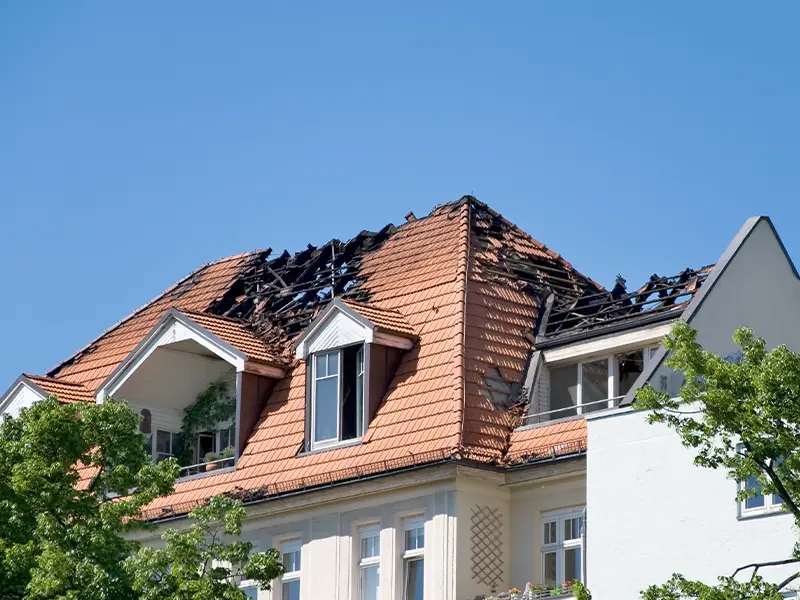 Roof of a building with extensive fire damage and missing tiles under a clear blue sky. fire damage restoration