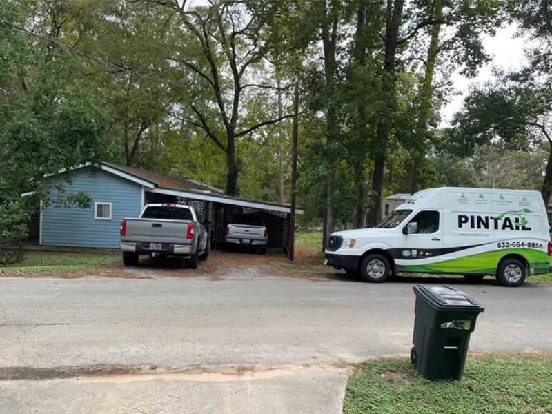 Two pickup trucks parked near a blue house with a carport and a white Pintail service van on the street. water damage restoration company