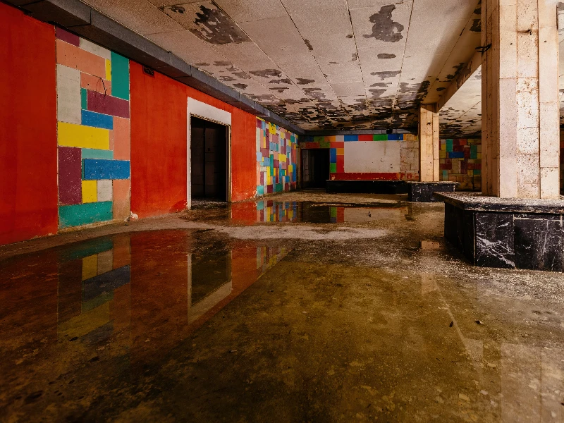 Abandoned room with colorful tiled walls, peeling ceiling, and water reflecting the interior. sewage cleanup services