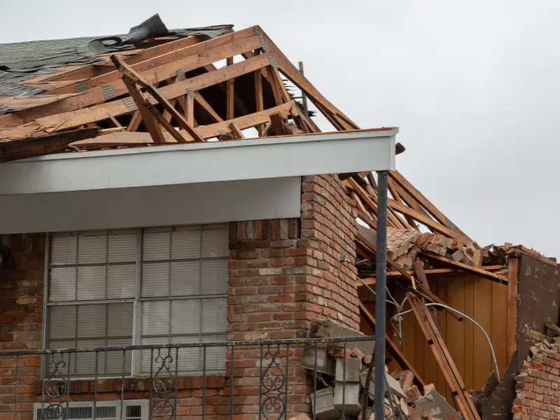 Partially collapsed brick house with exposed wooden roof framing and debris. storm damage restoration